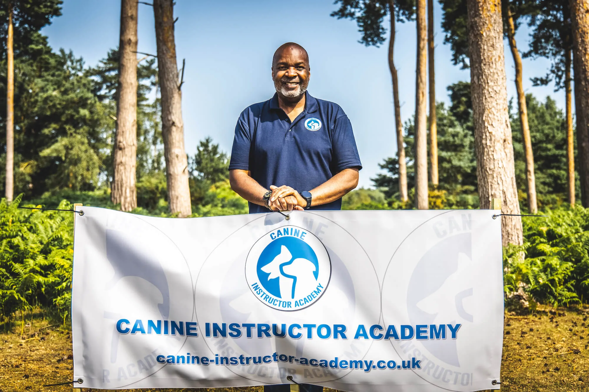 Photograph of Rob Alleyne stood behind a Canine Instructor banner